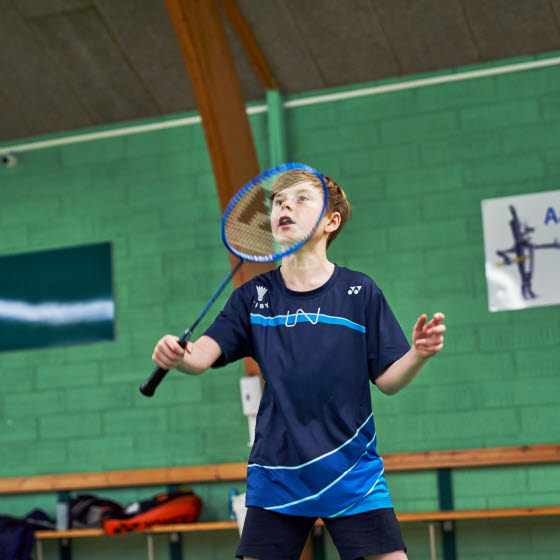 Dreng spiller badminton i hal
