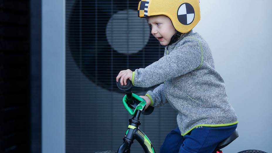 Lille dreng på sin cykel foran en varmepumpe